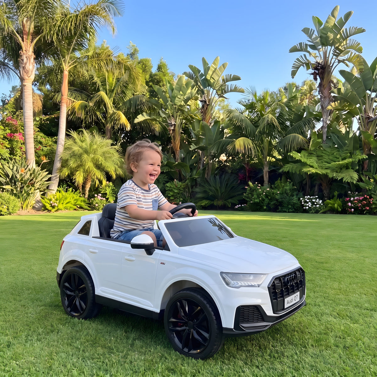 Enfant au volant de l'Audi Q7 blanche électrique dans un jardin
