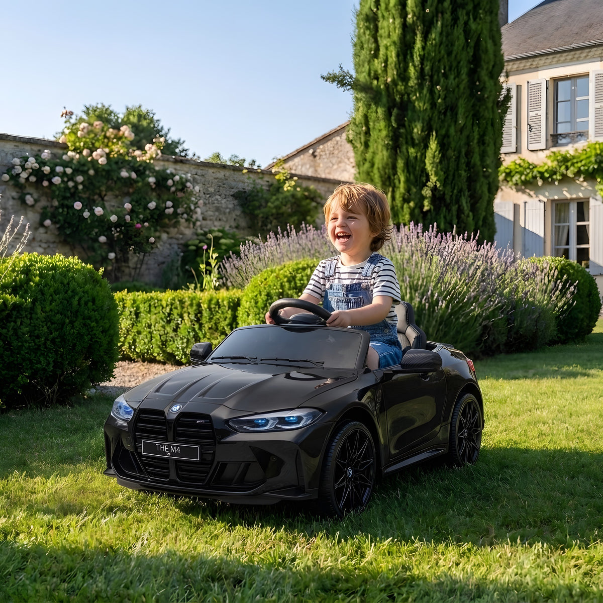 Enfant au volant de la BMW M4 noire électrique dans un jardin