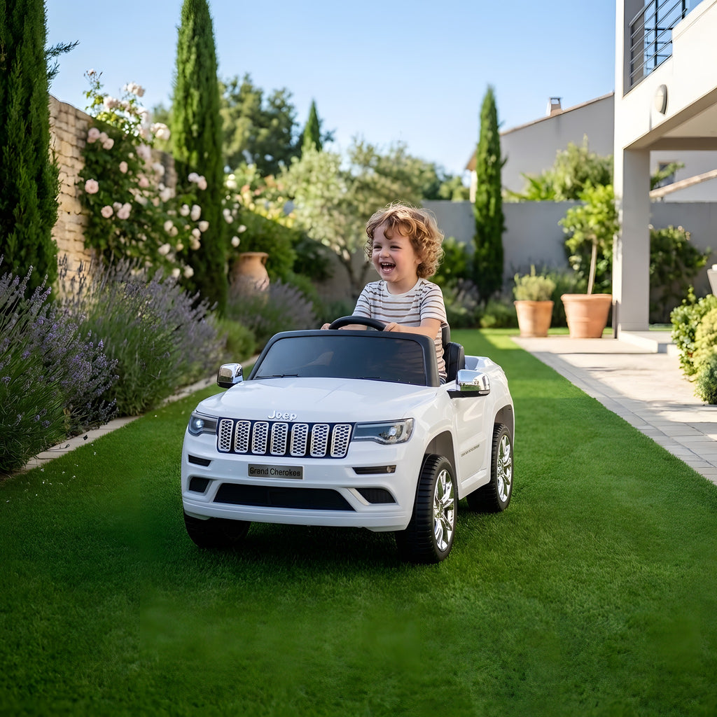 Enfant au volant de la Jeep Grand Cherokee blanche électrique dans un jardin